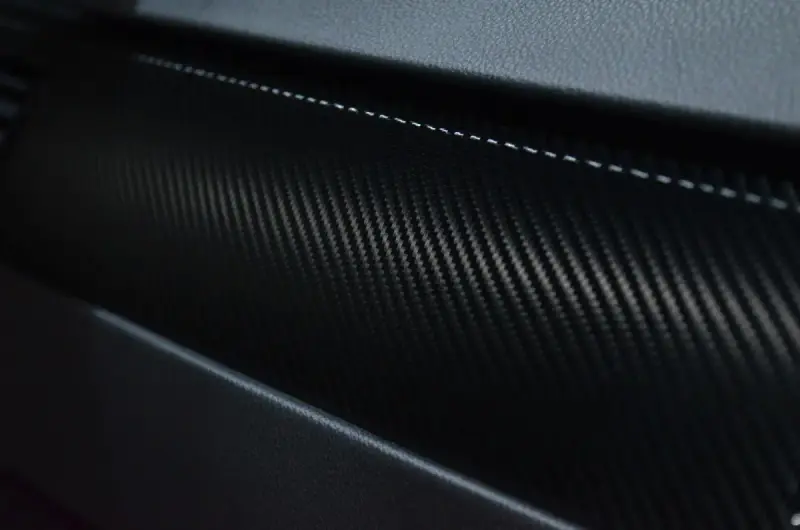 Close view of a dark carbon-fiber-patterned automotive surface.