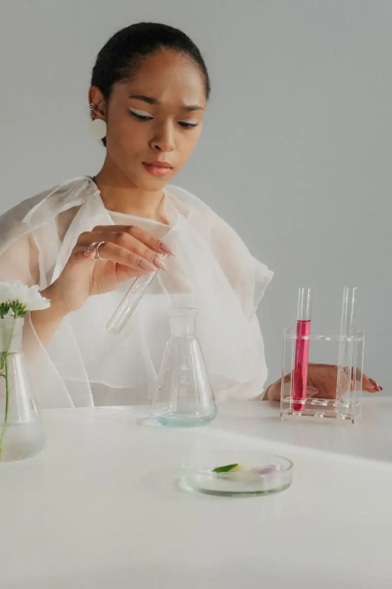 Woman in a sheer white top preparing test tubes and a petri dish