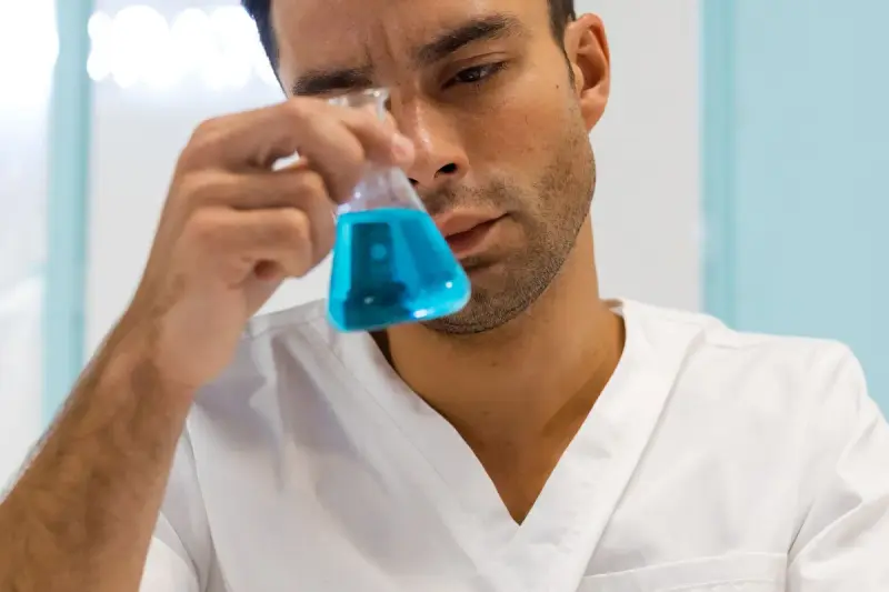 Man in a white coat studying a flask of blue liquid up close
