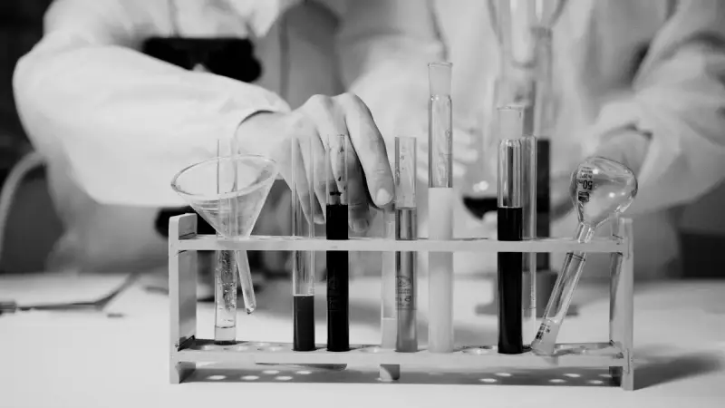 Black and white close-up of a hand working at a rack of test tubes and a funnel