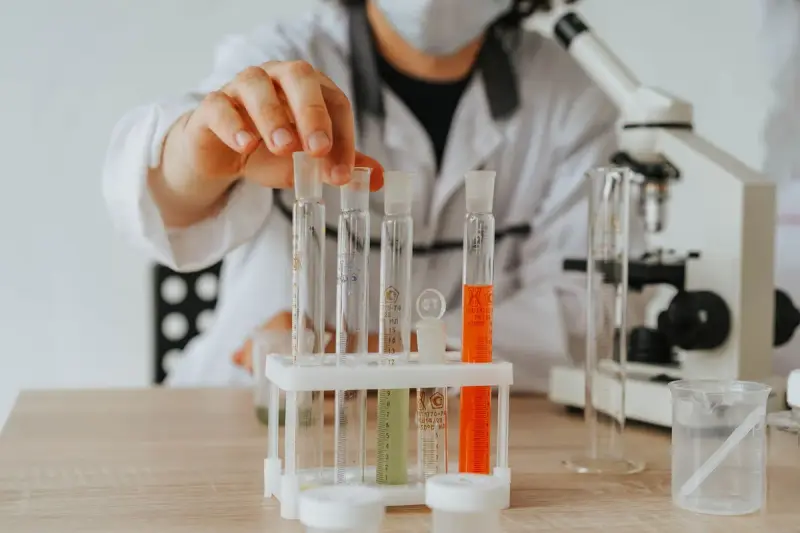 Hand placing a test tube in a rack of colored samples beside a microscope