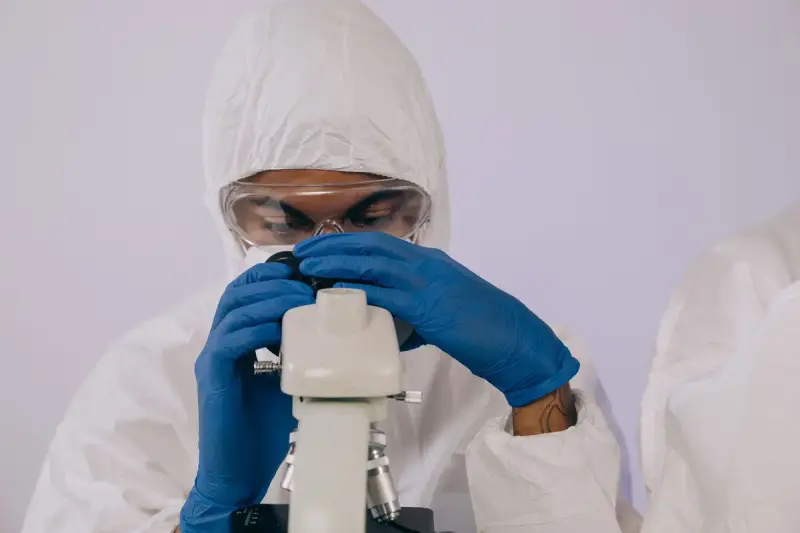Researcher in a protective suit and goggles looking into a microscope