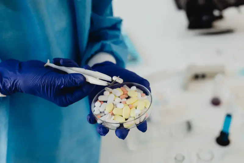 Gloved hands using tweezers to sort assorted pills in a petri dish