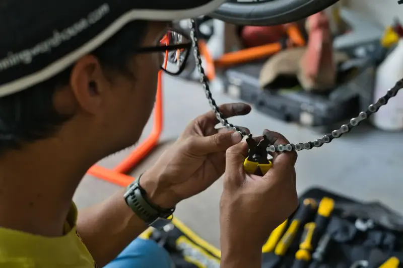 Mechanic's hands working a chain tool on a bicycle chain in a workshop
