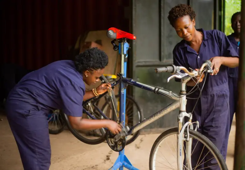Two women mechanics in blue overalls servicing a bicycle on a repair stand