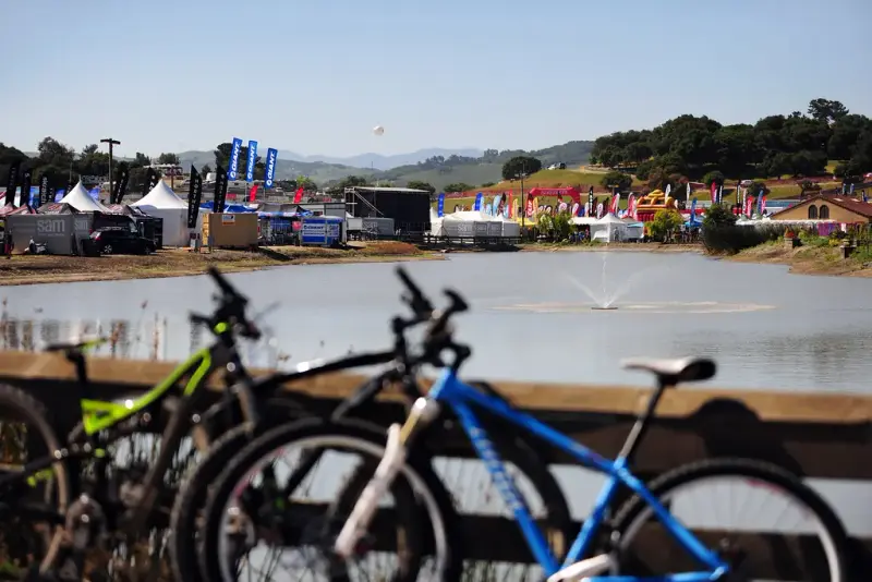 Expo tents and banners around the lakebed pond at Laguna Seca with mountain bikes parked in front
