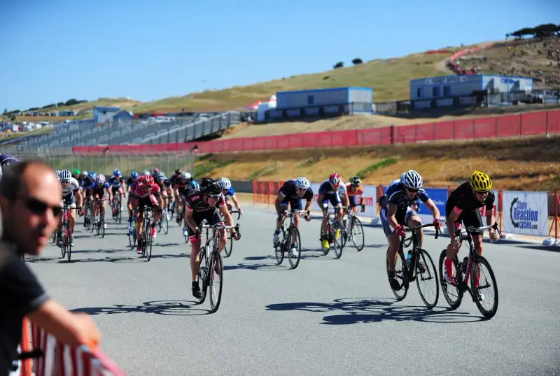 Road racers sprinting on the Laguna Seca raceway with dry hills and grandstands behind