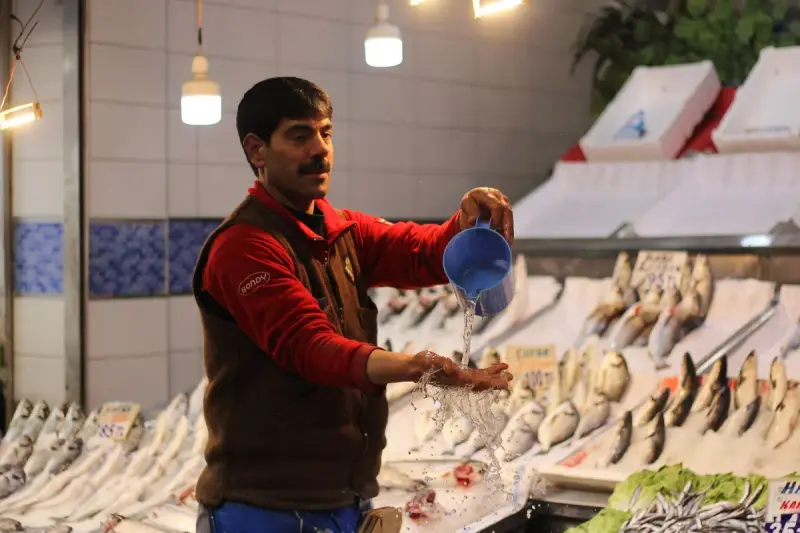 Fishmonger pouring water over whole fish on an iced display to keep them fresh
