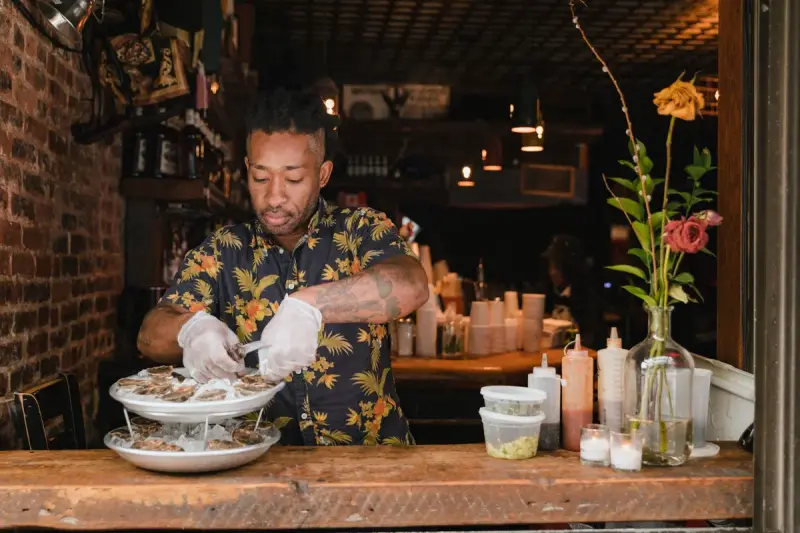 Man in gloves shucking fresh oysters onto a tiered ice platter at an oyster bar