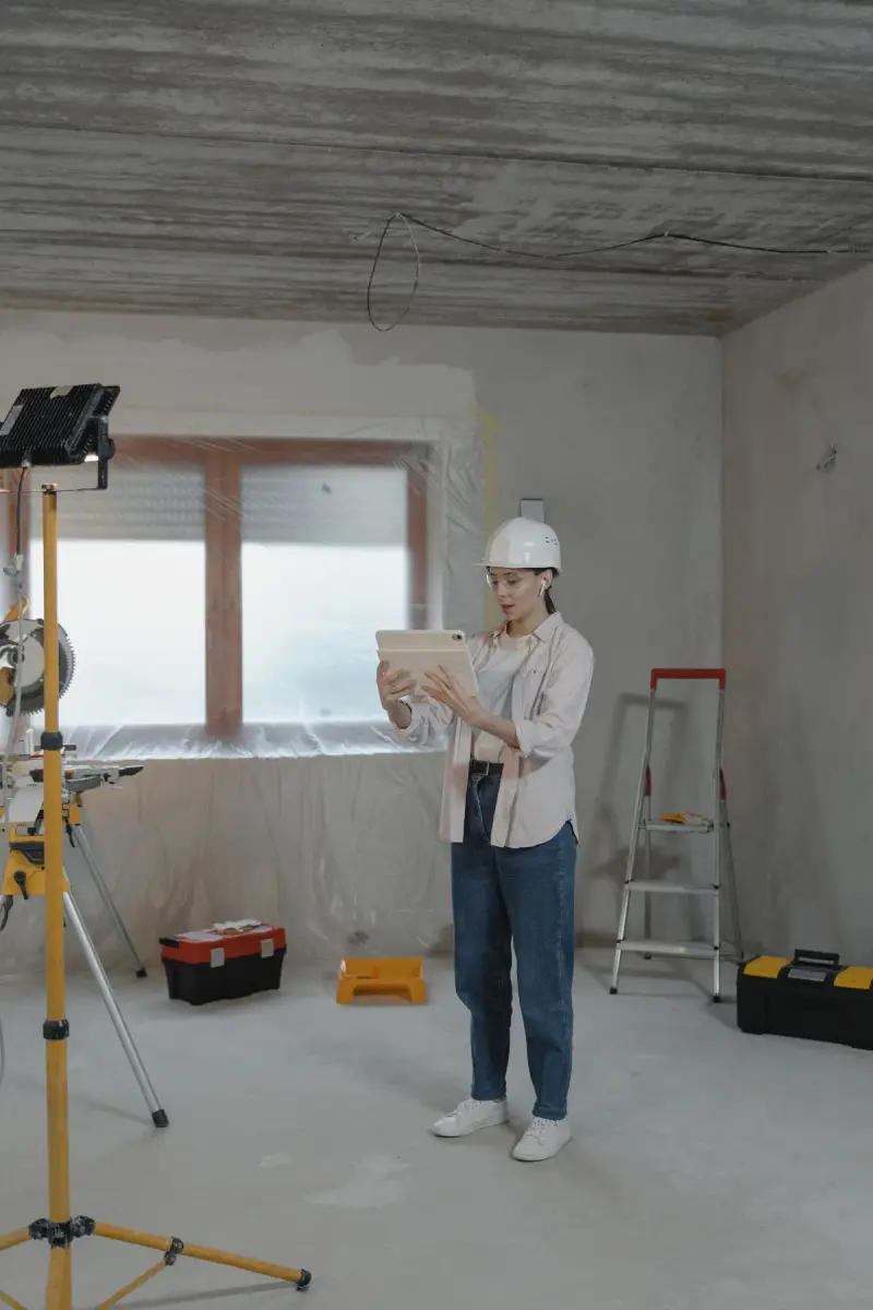 Woman in a white hard hat reviewing plans on a tablet inside a house under renovation