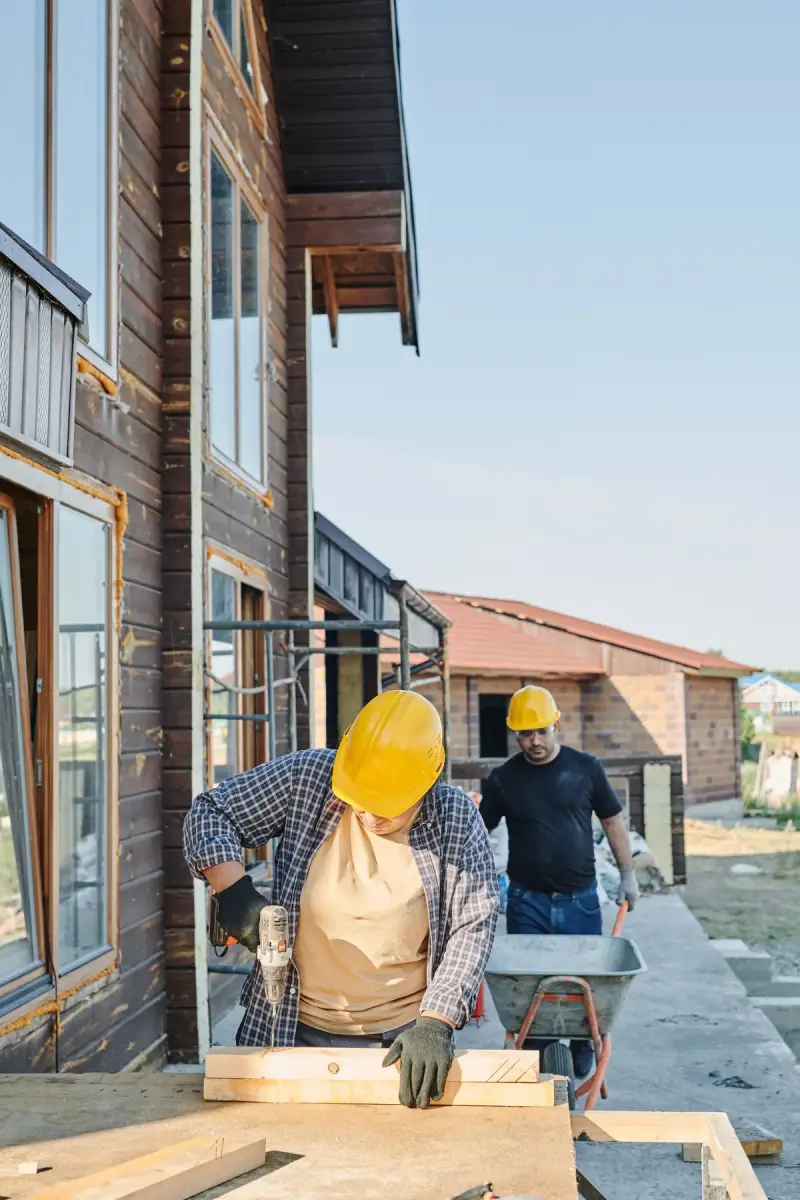 Two workers in hard hats doing carpentry on a wooden house frame