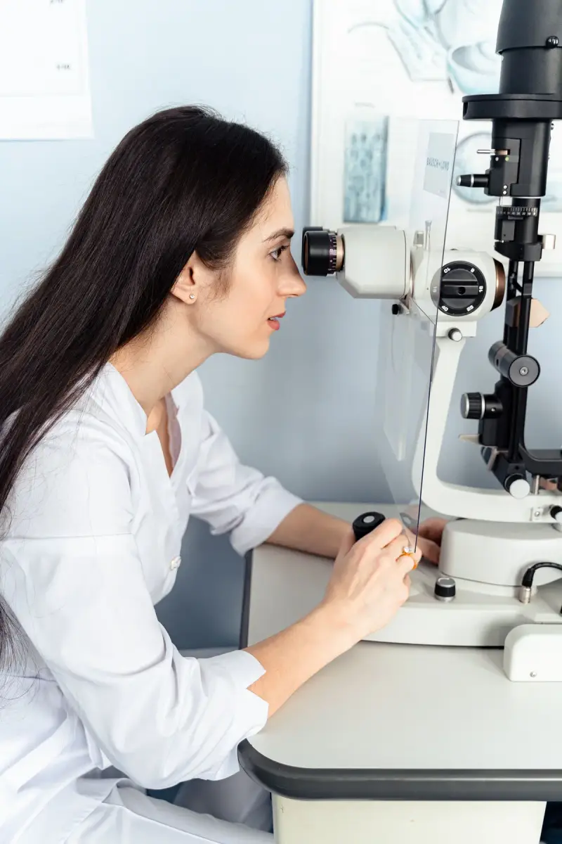 Optometrist in a white coat looking through a slit lamp in an eye clinic