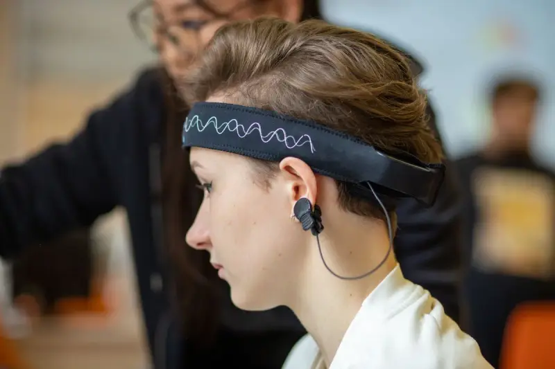 Young woman wearing a wireless EEG headband with an ear sensor while focused on a task