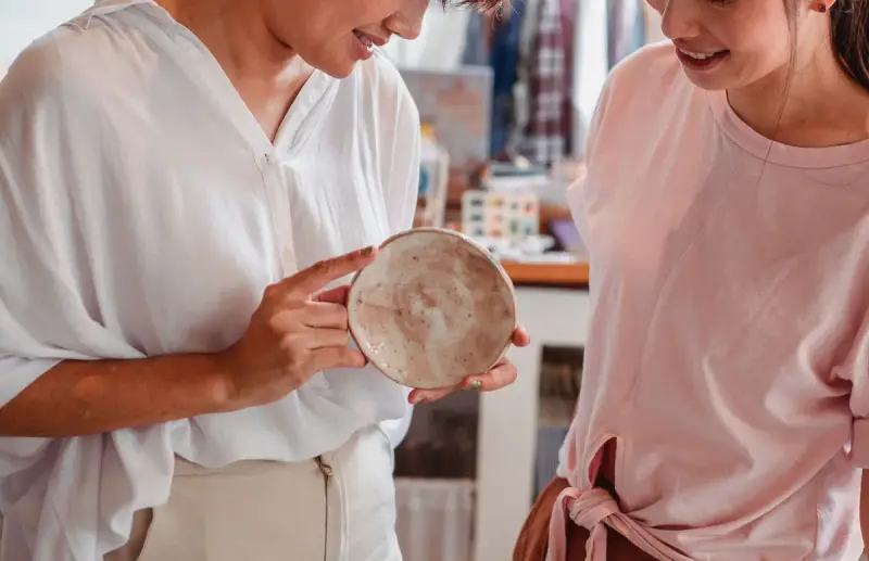 Two women smiling as they choose a ceramic plate in a home goods shop