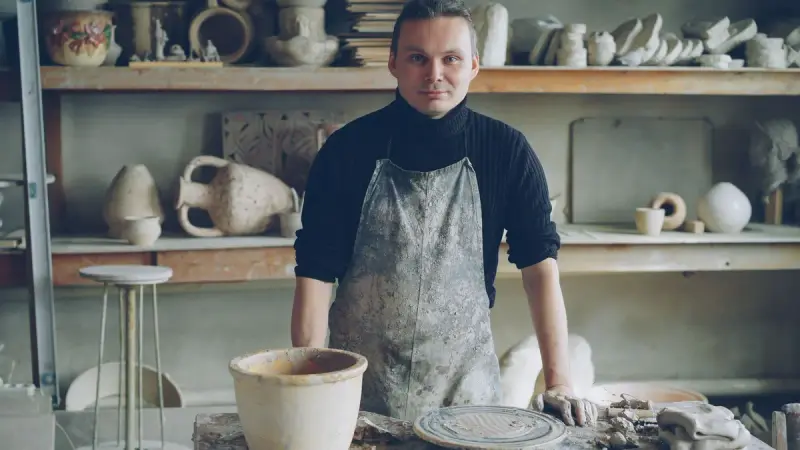 Craftsman standing in a pottery studio surrounded by shelves of handmade ceramics