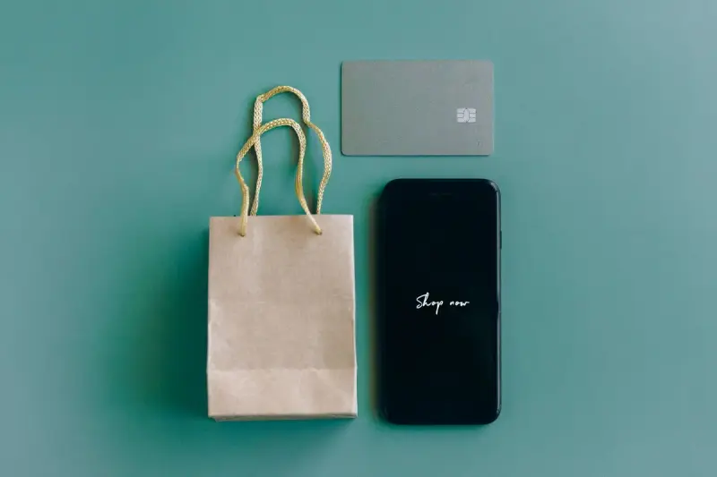 Smartphone, payment card and kraft paper shopping bag laid out on a green surface