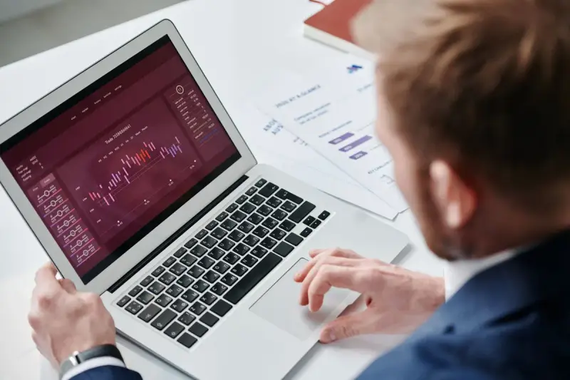 Businessman reviewing a sales analytics dashboard on a laptop with printed charts