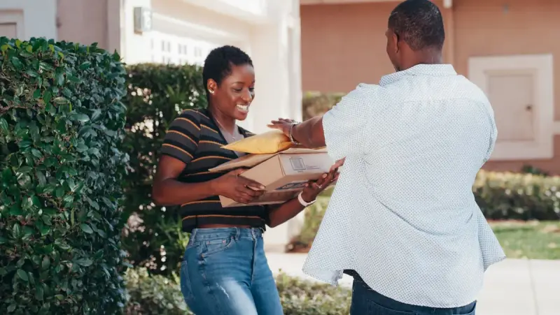 Smiling woman receiving a stack of parcels from a delivery driver outdoors