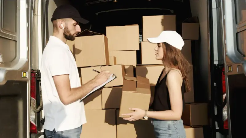 Two couriers checking parcels and a clipboard at the back of a loaded delivery van