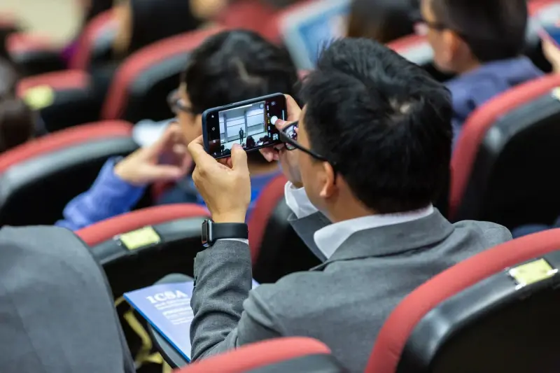 Conference attendee photographing the presentation screen with a smartphone from his seat