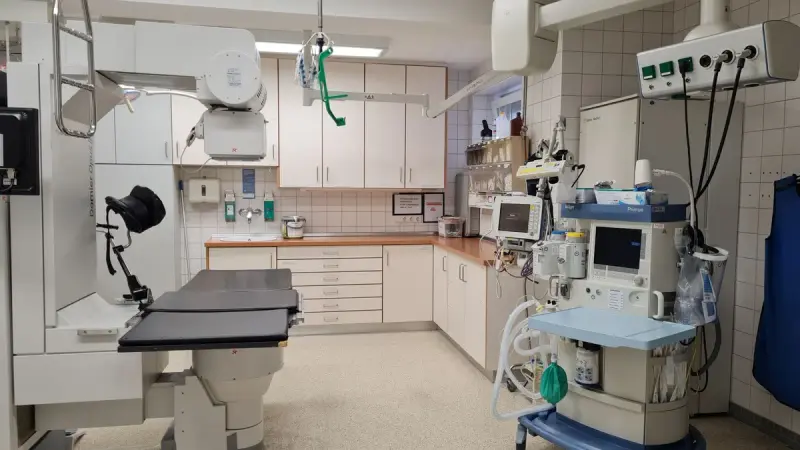 Hospital procedure room with a ceiling-mounted X-ray arm, procedure table and anesthesia cart