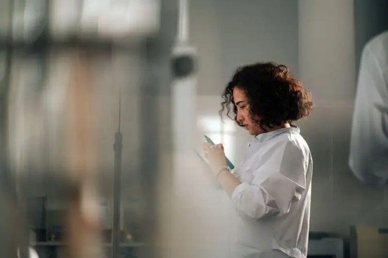 Female scientist with curly hair writing notes while standing in a laboratory