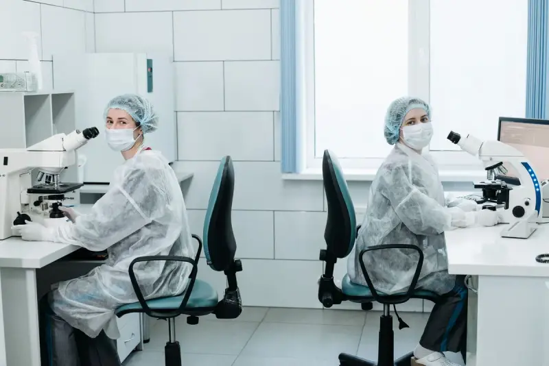 Two women scientists working side by side at laboratory microscopes
