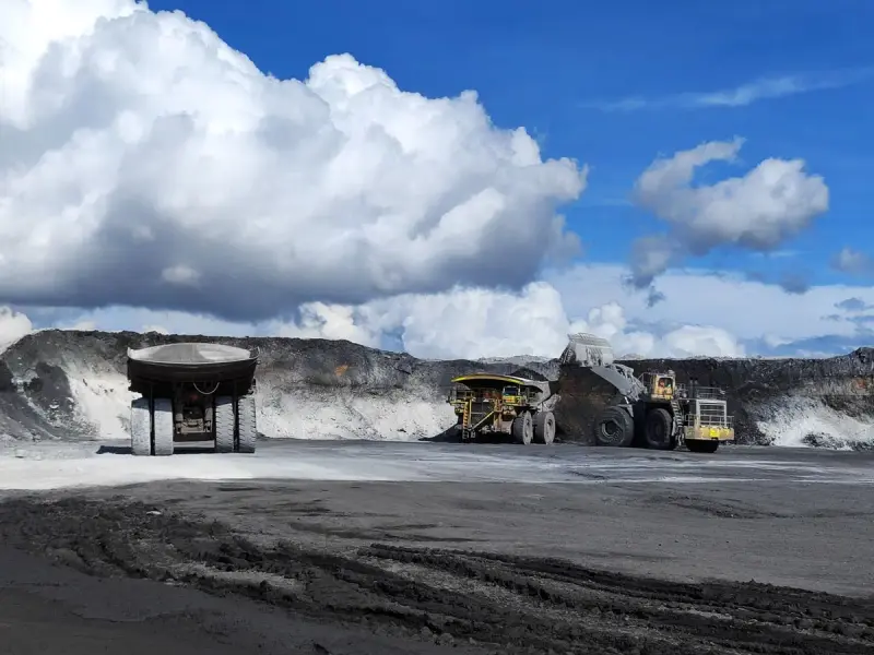 Open-pit mine with haul trucks and excavators working the benches under a blue sky