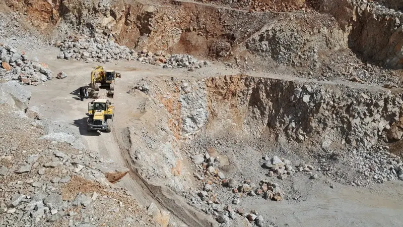 Wheel loader and excavator working a haul road between rock benches in an open-pit quarry