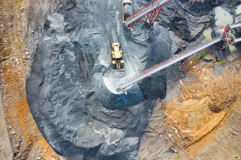 Aerial view of a loader beside dark stockpiles fed by long conveyor belts at a mine site