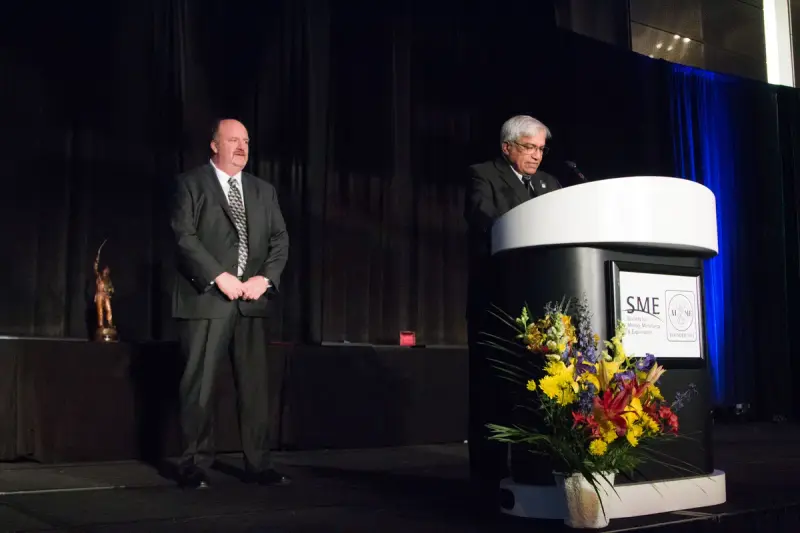 Two men on a stage beside a podium bearing the SME logo during an awards program