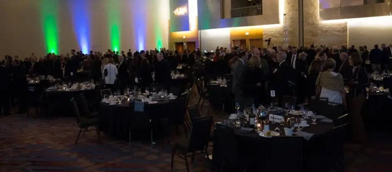 Ballroom filled with guests at round tables under colored wall lighting