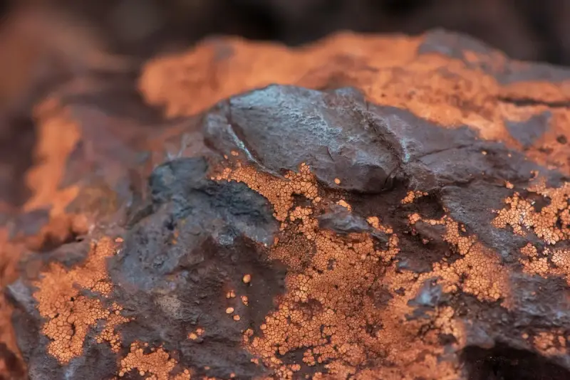 Macro view of dark iron ore rock crusted with rust-orange mineral grains
