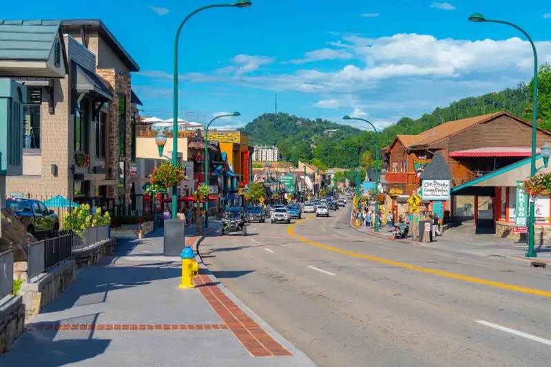 Sunny main street in Gatlinburg with storefronts and wooded hills behind