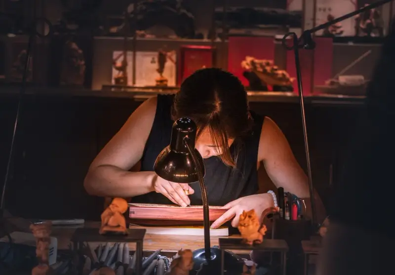 Artisan engraving a wooden piece by hand under a warm workshop lamp