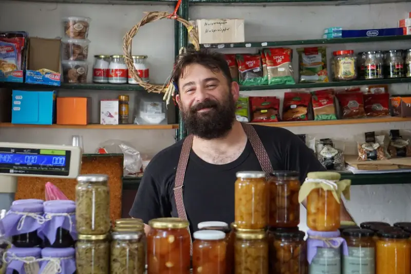 Smiling shopkeeper standing behind shelves of homemade jams and preserves