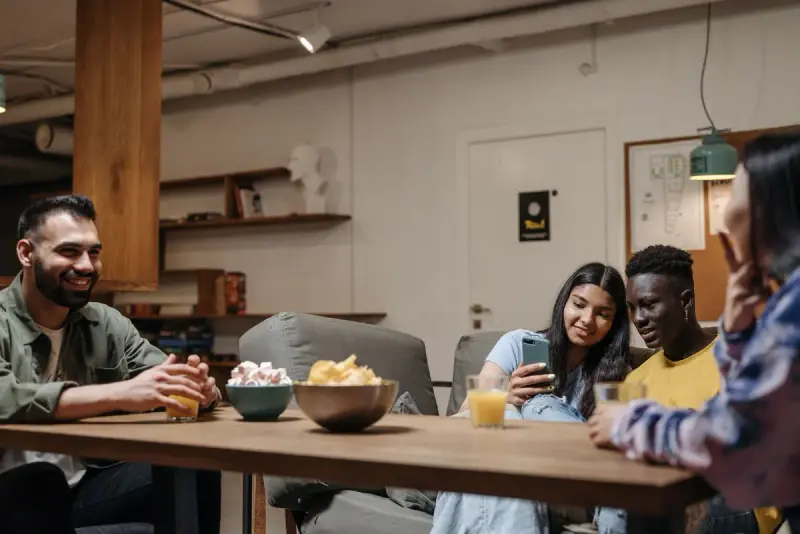 Group of smiling friends share bowls of snacks and glasses of juice around a wooden table