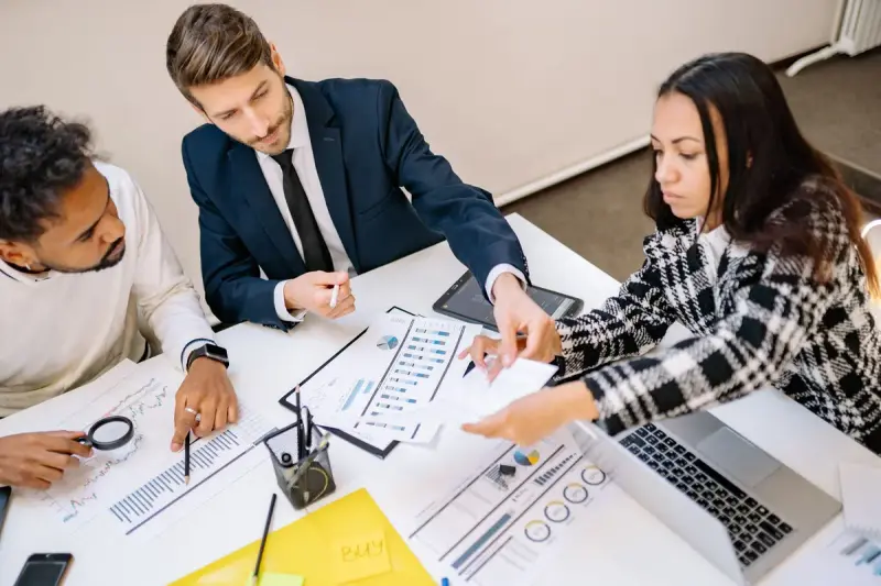 Professionals collaborating around a table covered in charts and documents
