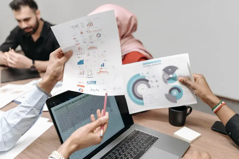 Hands holding printed graphs and data sheets beside a laptop