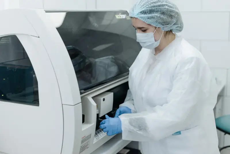 Scientist in protective gown and cap loading samples into a large automated lab analyzer
