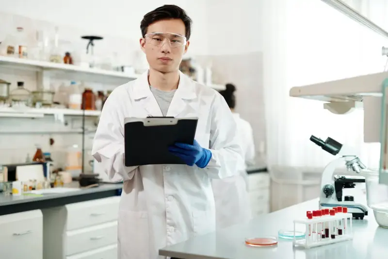 Scientist with a clipboard standing among shelves of reagents and lab equipment