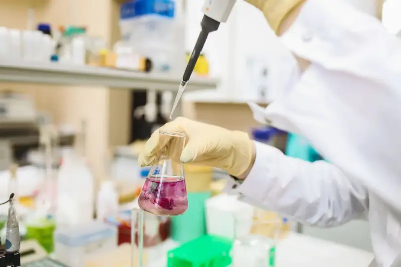 Pipette dispensing into a flask of pink liquid at a lab bench