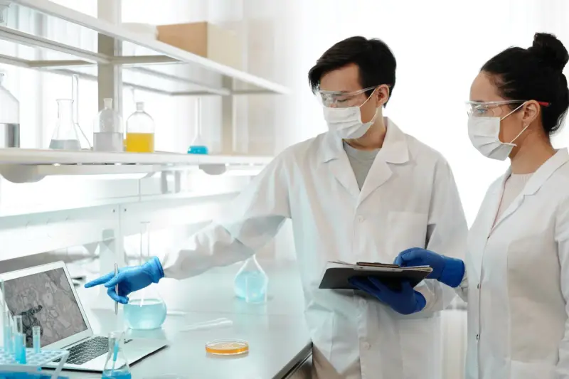Two masked scientists in lab coats examining data in a research laboratory