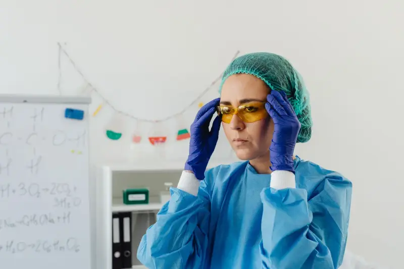 Woman in protective gown and hair cap putting on safety goggles in a lab