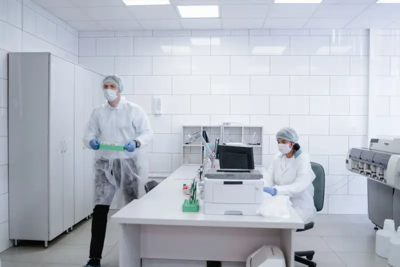 Two lab workers in protective gowns and caps in a clean white laboratory