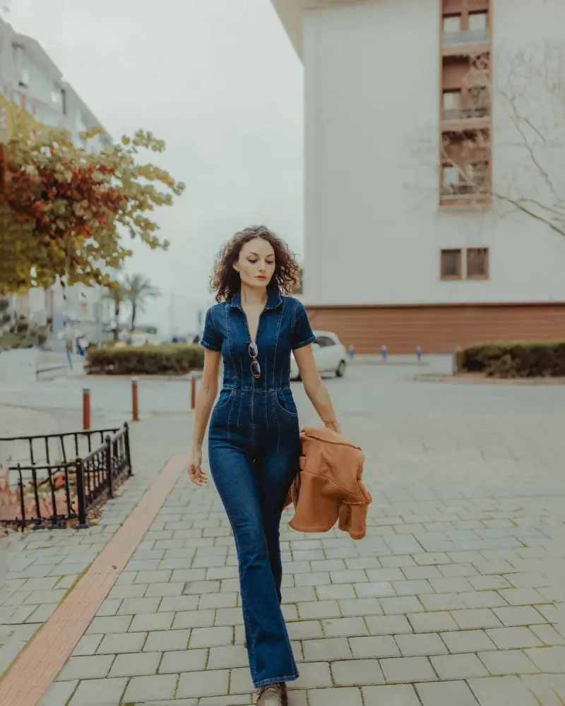 Woman walking down a city sidewalk in a fitted denim jumpsuit
