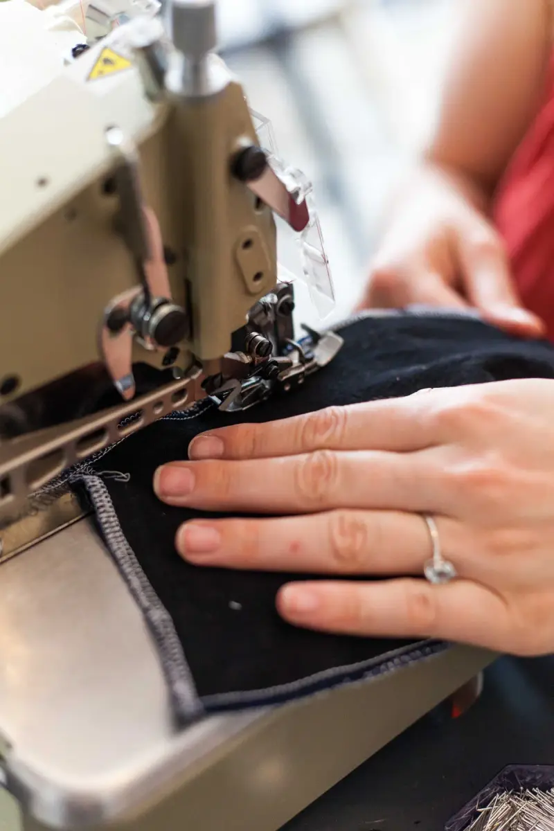 Hand guiding dark fabric through an industrial sewing machine