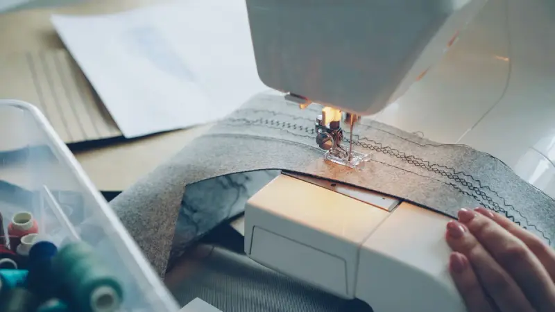 Close-up of a sewing machine stitching gray fabric beside spools of thread