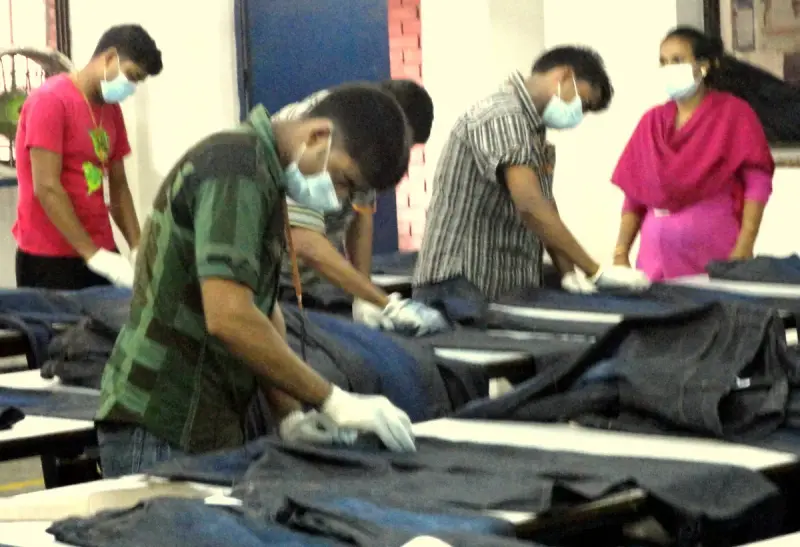 A worker hand-sanding denim jeans to create a worn finish