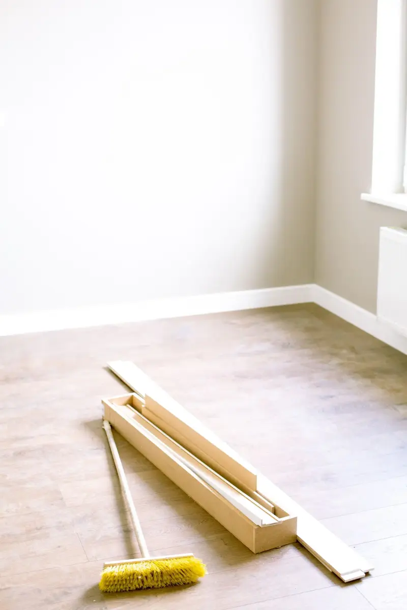 Empty room with wooden floor planks and a broom ready for renovation
